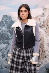 Chaleco de cuero sintético negro con interior y cuello de piel sintética blanca, cierre frontal y cintura elástica ajustada.