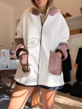 Campera tipo hoodie confeccionada en tejido de corderito sintético con diseño de bloques geométricos en tonos marrón, rosado y blanco. Presenta capucha amplia, corte oversize y mangas largas.