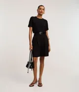 Blusa blanca de poliéster con cuello redondo, mangas cortas, cierre trasero en forma de gota, pequeñas aberturas laterales y acabados en pespuntes en las mangas y el cuello.