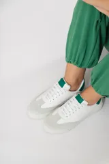 Zapatillas acordonadas de cuero color blanco con puntera de gamuza gris y detalles en verde.