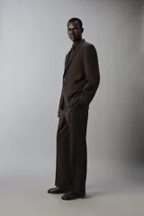 Pantalón de traje flare fit para hombre, confeccionado en tejido con lana, en color marrón oscuro. Presenta tiro medio, trabillas para cinturón, cierre frontal con cremallera y botón, bolsillos laterales y raya central marcada en las perneras.
