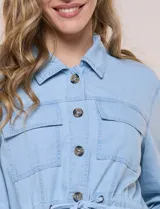 Sobrecamisa azul de denim de algodón liviano, con cuello camisero, cierre frontal de botones, bolsillos con solapa en el pecho y cordón ajustable en la cintura.