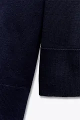 Jersey de punto liso, color azul brillante, con cuello redondo y manga larga. Presenta acabados en rib en puños, cuello y bajo, con aberturas laterales en el ruedo.