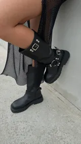 Botas de cuero negro de caña media con suela track, hebilla superior y arnés con tachas plateadas.