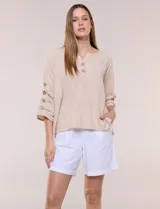 Blusa de algodón color beige, con cuello en V, cierre frontal con botones de madera y mangas cortas decoradas con una hilera de botones laterales.