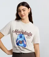 Remera de algodón color crema con cuello redondo y manga corta. Presenta un estampado frontal con el personaje Stitch sosteniendo una taza de café y la leyenda 'Coffee Mornings Club'.