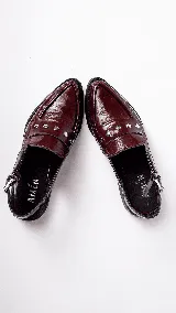 Mocasines tipo slingback de cuero charolado negro, con taco bajo de 1.5 cm y tira frontal decorada con tachas metálicas. Presenta una tira ajustable con hebilla en el talón.