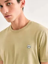 Camiseta blanca de algodón con cuello redondo y mangas cortas. Estampa rectangular con borde negro que contiene la frase "NATURAL ATMOSPHERE" en letras mayúsculas y una imagen de montañas y mar.