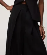 Pantalón de sastrería color negro, con cintura estructurada, pliegues delanteros, corte recto y cierre asimétrico.