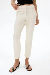 Pantalón tobillero cigarette de color beige en tejido elástico, con cintura estándar, bolsillos al bies y piernas ajustadas con raya marcada.