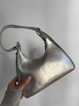 Cartera baguette plateada con textura craquelada, asa corta y logo "Fashion & Bag" en el frente.