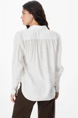 Camisa blanca de corte relajado, con cuello clásico, cierre frontal de botones y mangas largas amplias con puños ajustados.