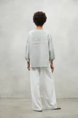 Buzo oversize color gris claro, con cuello redondo, hombros caídos y puños ajustados. Confeccionado con 50% algodón orgánico y 50% algodón reciclado.