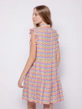 Vestido corto con estampado floral multicolor, cuello tipo camisa y cierre frontal con botones. Presenta volados en las sisas y un diseño de falda con volados en el ruedo.