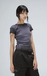 Remera baby tee de manga corta y cuello redondo, confeccionada en tejido ribb de algodón. Presenta un corte ajustado al cuerpo con costuras visibles en los hombros y un acabado de borde crudo en el ruedo.