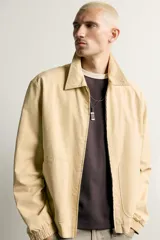 Cazadora regular fit de color beige, confeccionada en mezcla de algodón y lyocell. Cuenta con cuello camisero, cierre frontal de cremallera, bolsillos de plastrón en la cadera, mangas largas con puños elásticos y bajo con ajuste elástico.