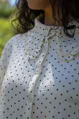 Camisa crop de muselina color blanco con lunares negros, corte amplio, cuello con volados y botones frontales.