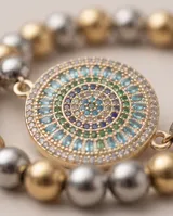 Pulsera de acero con baño de oro, compuesta por esferas metálicas en tonos dorados y plateados, con un dije central redondo decorado con cristales multicolor.
