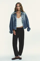 Pantalón negro de tiro medio con pinzas frontales, bolsillos laterales y falsos bolsillos de vivo en la espalda. El bajo termina en puño elástico.