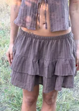 Falda corta color marrón con diseño de volados escalonados y short interior incorporado. Presenta una textura sutilmente rayada y una silueta liviana y fluida.