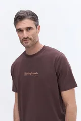 Remera de manga corta color azul grisáceo con cuello redondo y calce regular. Presenta un estampado gráfico en la espalda que combina una cafetera italiana con flores y el texto Sunday Brunch.