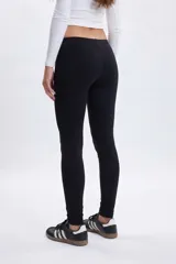 Legging de corte ajustado en color negro, confeccionado en tejido elástico de tiro medio.