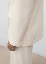 Chaqueta de traje color beige, con cuello de solapa, cierre cruzado con un botón y bolsillos con solapa en los laterales y en el pecho.