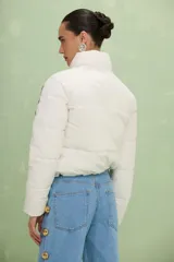 Campera puffer color blanco off-white con diseño acolchado, cuello alto y cierre frontal con botones a presión. Presenta bordados florales en tonos violeta, amarillo y rosa en la parte frontal y mangas.