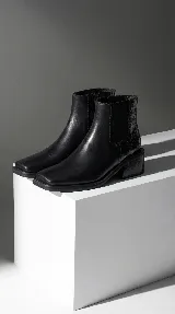 Bota corta tipo chelsea de cuero vacuno color negro, con puntera cuadrada, taco cuadrado de madera y detalle de textura grabada en el panel elástico lateral.