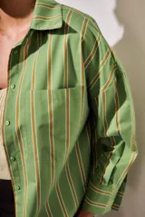 Camisa de corte oversize con estampado de rayas verticales en tonos verde, blanco y ocre. Presenta cuello clásico, cierre frontal con botones, bolsillo en el pecho y mangas largas con puños abotonados.