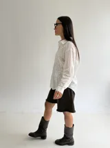 Camisa blanca de manga larga con bordados florales al tono en el frente, cuello clásico y cierre frontal de botones.