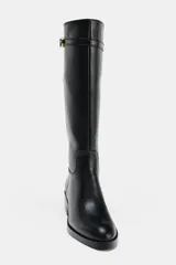 Bota de caña alta estilo hípica en color negro, con detalle de tira decorativa con hebilla metálica en la parte superior. Presenta tacón bajo ancho y punta redonda.