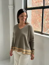 Sweater de punto en color verde oliva, con cuello en V y diseño holgado. Presenta detalles de franjas en color beige en el cuello, los puños y el ruedo.