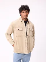 Sobrecamisa de pana color beige, con cierre frontal de botones a presión, dos bolsillos frontales con solapa y bolsillos laterales. Presenta cuello clásico y diseño acolchado con forro interior.