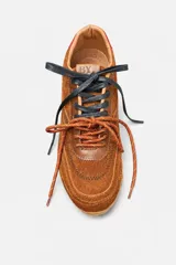 Championes de gamuza color marrón con detalles en cuero liso del mismo tono. Presentan cordones bicolores en naranja y negro, suela de goma plana y un detalle en color rojo en la parte trasera del talón.