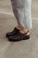 Zueco de cuero marrón oscuro, con diseño cerrado en la parte delantera, tira ajustable en el talón con hebilla metálica y taco bajo cuadrado.