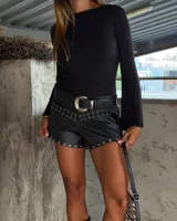 Short negro de tiro bajo, con acabado que simula cuero o vinilo, decorado con ojales metálicos plateados a lo largo del ruedo y en la parte superior delantera.