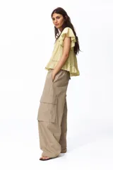 Blusa de tejido liviano color amarillo claro, con escote en V profundo, mangas cortas estilo mariposa y cierre frontal con botones. Presenta detalles de alforzas e inserciones de encaje en el frente y en el borde del ruedo y las mangas, terminando en un volante inferior.