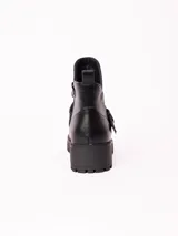 Bota corta de cuero sintético color negro, con suela track de goma y detalle de tira con hebilla metálica en el tobillo.