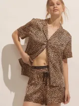 Pijama corto de satín con estampado animal print de leopardo. Incluye una camisa de manga corta con botones frontales, cuello solapa y ribetes negros, junto con un short con cintura elastizada y cordón ajustable.