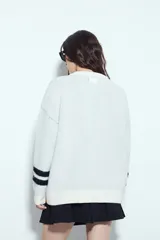 Sweater de punto color blanco con estampado numérico '87' en color negro en el frente y detalles de rayas horizontales en las mangas. Presenta cuello redondo y un corte relajado.