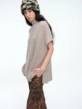 Chaleco tipo poncho de tejido de punto color beige, con cuello alto tipo polera, diseño holgado y aberturas laterales.