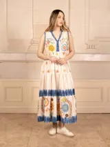 Vestido largo color crema con estampado de flores y corazones en tonos azules, naranjas y amarillos. Tiene cuello en V con ribete azul y corte imperio con falda escalonada.