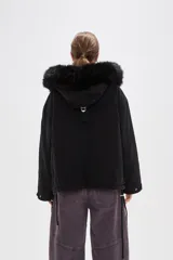 Campera negra de algodón con capucha, cierre frontal oculto y bolsillos laterales. Presenta un diseño holgado con detalles de piel sintética en el borde de la capucha.