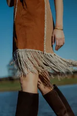 Vestido corto negro sin mangas, con escote en V y detalle de flecos en el ruedo. Presenta bordados en color blanco en el escote, los bolsillos y el centro del vestido.