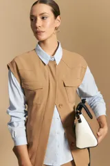 Chaleco negro de corte estructurado con cuello redondo, cierre frontal oculto y lazo ajustable en la cintura. Presenta dos bolsillos frontales con solapa y diseño de hombros caídos.