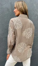 Camisa de seda color visón con bordados en relieve de hojas grandes, cuello camisero, mangas largas y cierre frontal con botones.