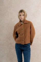 Chaqueta corta tipo blazer color marrón, confeccionada en tela de lana afieltrada. Tiene cuello camisero, silueta cuadrada, cierre frontal con botones y bolsillos delanteros.