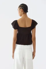 Blusa marrón de punto pointelle con textura, escote corazón, detalle cut-out con cordón de ajuste en el busto, mangas cortas circulares con volados y diseño acampanado.
