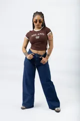 Remera ajustada de manga corta color marrón oscuro, con cuello redondo y ribetes blancos en el cuello y mangas. Presenta un estampado frontal en blanco con el texto "MILANO" y un escudo con el número "96".